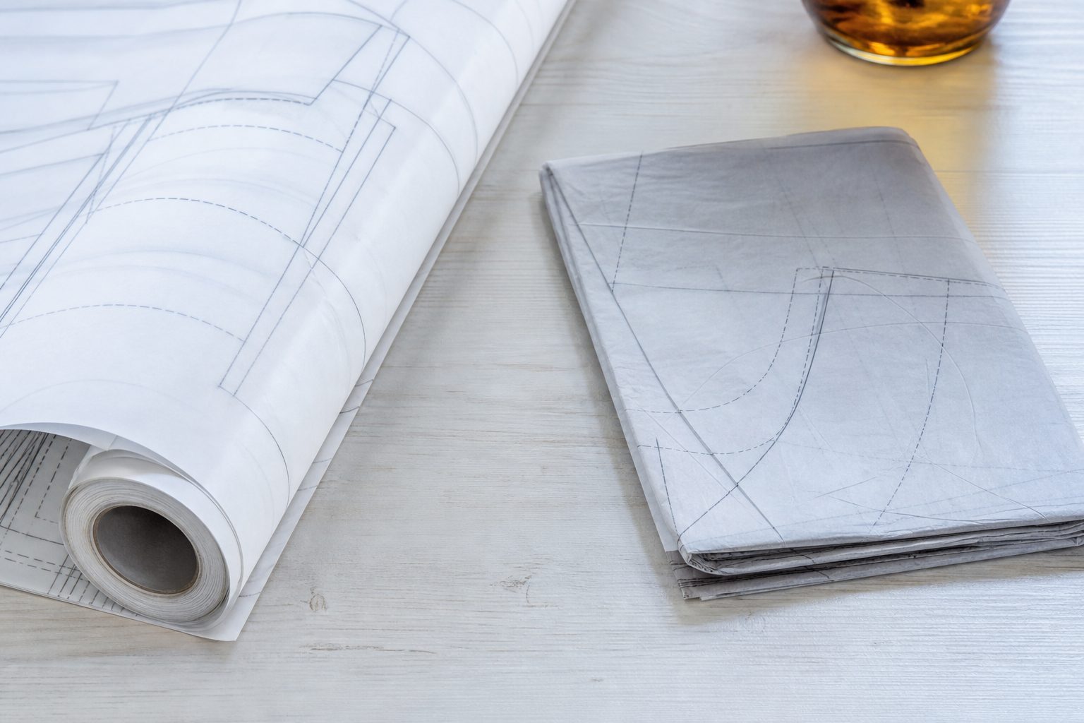 Rolled large format pattern sheet beside a folded tissue pattern on a pale wooden table
